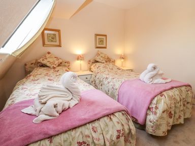 A bedroom with two single beds with floral bedspreads pink throws and towel swans at Rosemary Cottage in Bourton-on-the-Water