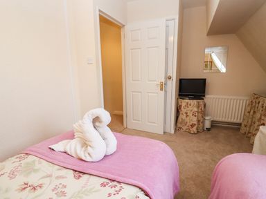 A bedroom with two beds covered in pink blankets and a towel folded in the shape of a swan on one bed at Rosemary Cottage in Bourton-on-the-Water