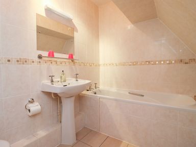 A bathroom with a bathtub a pedestal sink a mirror and tiled walls at Rosemary Cottage in Bourton-on-the-Water