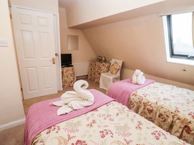A bedroom with two single beds pink blankets and towel swans a chair a small TV and a window at Rosemary Cottage in Bourton-on-the-Water