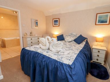 A bedroom with a double bed featuring blue and floral bedding and towel swans with bedside tables and lamps at Rosemary Cottage in Bourton-on-the-Water