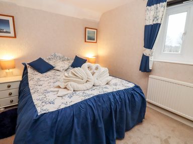 A bedroom with a bed covered with blue and white bedding and towels folded as swans Rosemary Cottage Bourton-on-the-Water