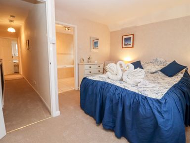 A bedroom with a bed covered in blue and white linens and two towel swans next to a dresser and open doorway at Rosemary Cottage in Bourton-on-the-Water