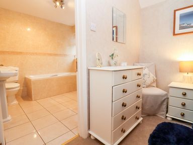 A bathroom with a bathtub and toilet next to a bedroom with a white dresser a chair a bedside table and a lamp at Rosemary Cottage in Bourton-on-the-Water