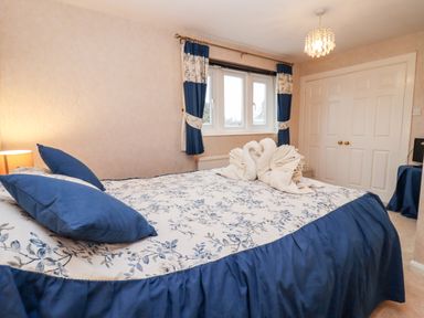 A bedroom with a bed covered by floral and blue bedding and two towel swans on it at Rosemary Cottage in Bourton-on-the-Water