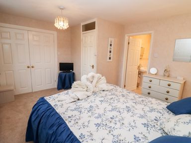A bedroom with a bed covered in floral bedding towels folded as swans on bed a dresser and a small television at Rosemary Cottage in Bourton-on-the-Water