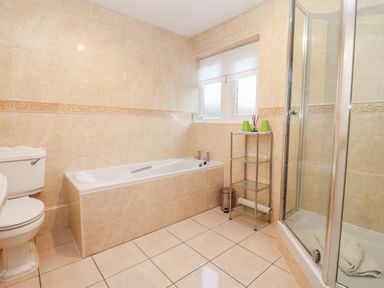 A bathroom with a bathtub toilet shower and a glass shelving unit at Rosemary Cottage in Bourton-on-the-Water