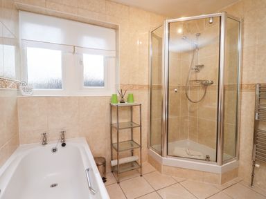 A bathroom with a bathtub shower enclosure glass shelf and window at Rosemary Cottage in Bourton-on-the-Water