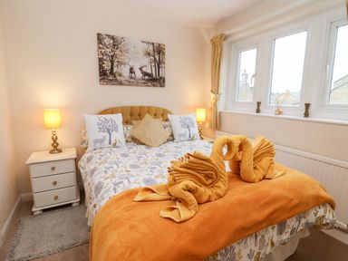 A bedroom with a double bed two bedside tables with lamps and windows at Rosemary Cottage in Bourton-on-the-Water