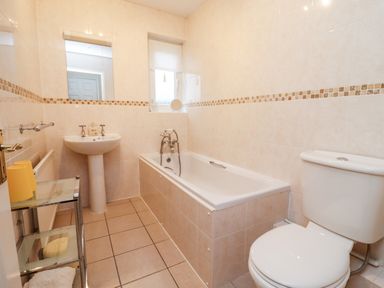 A bathroom with a bathtub sink toilet and glass shelves at Rosemary Cottage Bourton-on-the-Water
