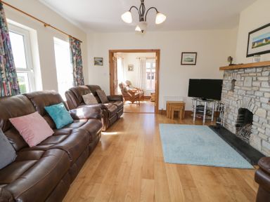 A living room with leather sofas cushions a stone fireplace a television and wooden flooring at Creeslough View in Creeslough near Glenveagh National Park County Donegal