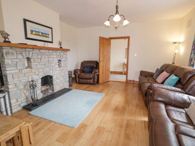 A living room with a stone fireplace leather armchairs and couch hardwood floors and a blue rug at Creeslough View Creeslough near Glenveagh National Park County Donegal