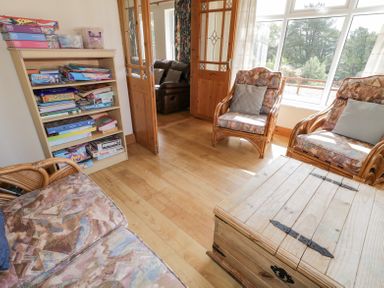 A sitting room with wooden furniture a bookshelf with board games and large windows at Creeslough View in Creeslough near Glenveagh National Park County Donegal