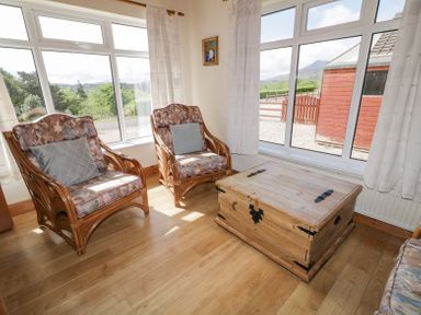 A sitting area with two wooden armchairs with patterned cushions a wooden chest and large windows at Creeslough View in Creeslough near Glenveagh National Park County Donegal