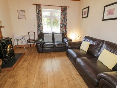 A living room with two leather sofas cushions a wood stove and window with curtains at Creeslough View Creeslough near Glenveagh National Park County Donegal