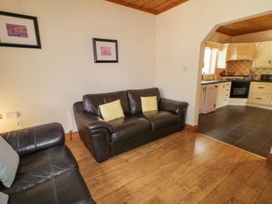A living room with two leather sofas and two framed pictures on the wall next to a kitchen with tiled floor at Creeslough View in Creeslough near Glenveagh National Park County Donegal