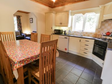 A kitchen with wooden chairs around a table covered with a colorful plastic tablecloth next to cream cabinets and a window at Creeslough View in Creeslough near Glenveagh National Park County Donegal