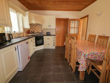 A kitchen with cream cabinets a dining table with colorful tablecloth and wooden chairs at Creeslough View Creeslough near Glenveagh National Park County Donegal