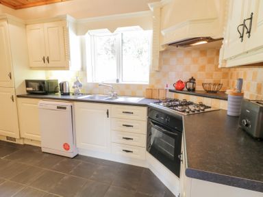 A kitchen with white cabinets black countertops a gas stove an oven a dishwasher a microwave a kettle a double sink and a window at Creeslough View Creeslough near Glenveagh National Park County Donegal