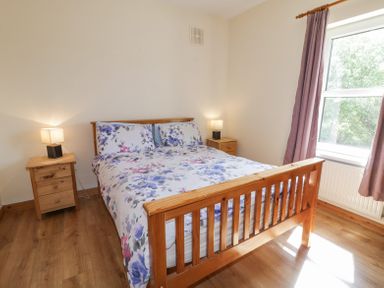 A bedroom with a wooden double bed floral bedding two bedside tables with lamps and a window with curtains at Creeslough View in Creeslough near Glenveagh National Park County Donegal