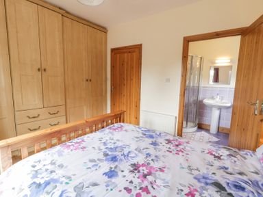 A bedroom with floral bedspread wooden wardrobe and an ensuite bathroom at Creeslough View in Creeslough near Glenveagh National Park County Donegal
