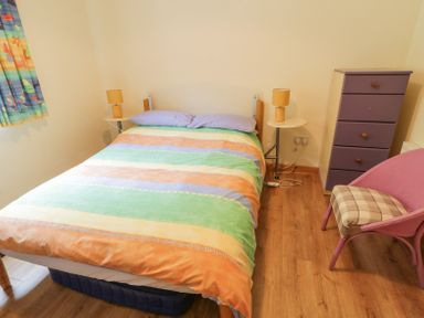 A bedroom with a bed with colorful striped bedding two bedside tables with lamps a purple chest of drawers a pink chair and a window with patterned curtains at Creeslough View in Creeslough near Glenveagh National Park County Donegal