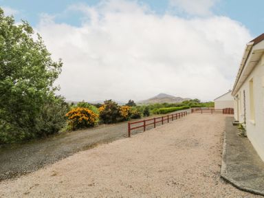 A gravel driveway with a low wooden fence next to a white house and trees with yellow flowers at Creeslough View in Creeslough near Glenveagh National Park County Donegal