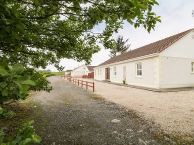 A gravel driveway leading to a single-story white house with a brown roof surrounded by trees at Creeslough View in Creeslough near Glenveagh National Park County Donegal