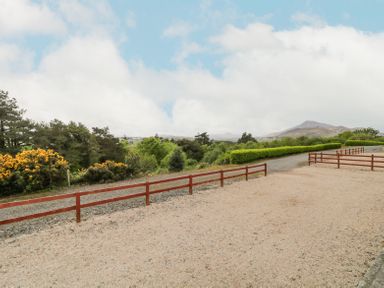 A gravel driveway with red wooden fences and green bushes with mountains in the background at Creeslough View in Creeslough near Glenveagh National Park County Donegal