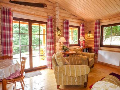A sitting area with armchairs wooden walls and red plaid curtains at Wilderness Lodge in Stiperstones