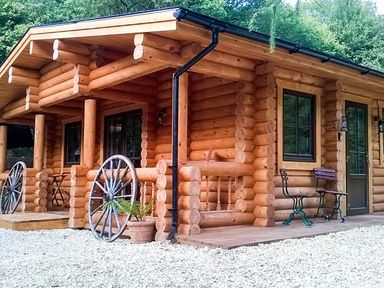 A wooden log cabin with a porch two large wagon wheels a potted plant and two metal benches at Wilderness Lodge in Stiperstones
