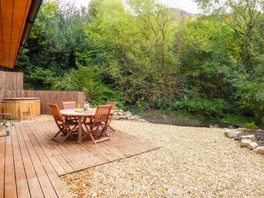 A wooden deck with a round table and chairs beside a hot tub in a garden at Wilderness Lodge in Stiperstones