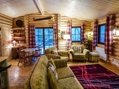 A living room with wooden walls chairs a table and a patterned rug at Wilderness Lodge in Stiperstones