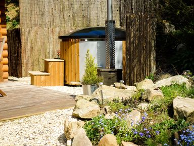 An outdoor area with wooden hot tub and steps surrounded by rocks and plants at Wilderness Lodge in Stiperstones