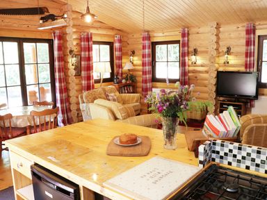 A kitchen island with a cake and flowers in a wooden cabin living room with red plaid curtains and a television at Wilderness Lodge in Stiperstones