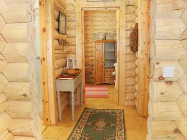 A wooden hallway with a small table and decorative items leading to a room with a wardrobe and chair at Wilderness Lodge in Stiperstones