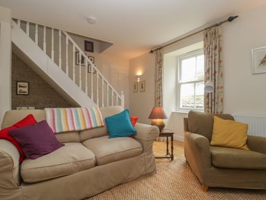 A living room with sofas and colorful pillows next to a staircase and window at Drovers in Sutton Mallet