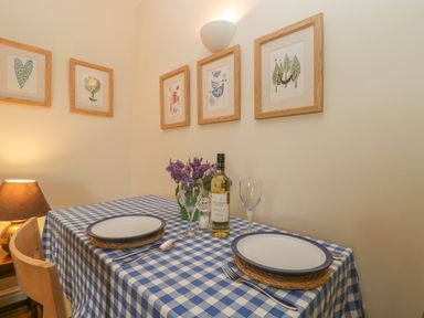 A dining table with blue and white checked tablecloth plates cutlery wine glasses and a bottle of wine with framed pictures on the wall at Drover's in Sutton Mallet