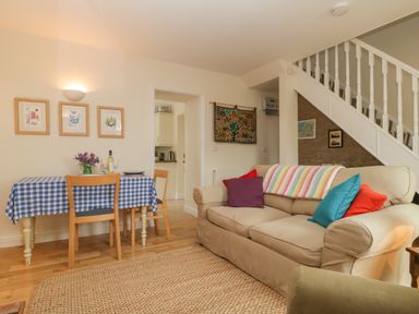 A living room with a beige sofa with colorful cushions a dining table with a blue checkered tablecloth and wooden chairs at Drover's in Sutton Mallet