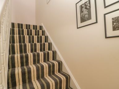 A staircase with a striped carpet and framed pictures on the wall at Drover's in Sutton Mallet