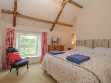 A bedroom with a double bed two blue blankets wooden dresser and a chair by a window at Drover's in Sutton Mallet