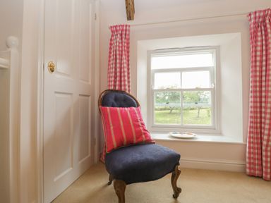A chair with a pink cushion by a window with checkered pink curtains at Drover's in Sutton Mallet