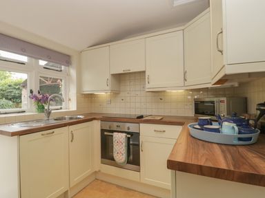 A kitchen with cream cabinets a wooden countertop a stainless steel oven and sink a microwave and a tray with blue tea set at Drover's in Sutton Mallet