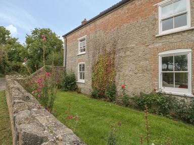 A stone house with white framed windows and a small garden with flowers behind a stone wall at Drover's in Sutton Mallet