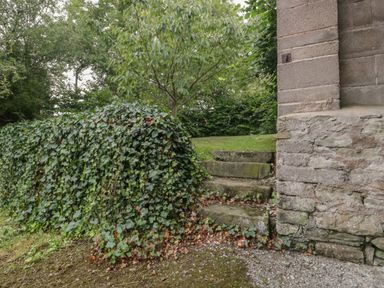 A small set of stone steps leading to a grassy area with a tree and ivy-covered stone wall next to a stone building at Drover's in Sutton Mallet