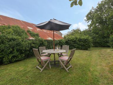 A garden with a round wooden table and four chairs with cushions under a large umbrella at Drover's in Sutton Mallet