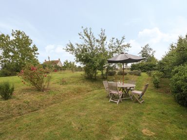 A garden area with trees shrubs and a round wooden table with chairs under a patio umbrella at Drover's in Sutton Mallet