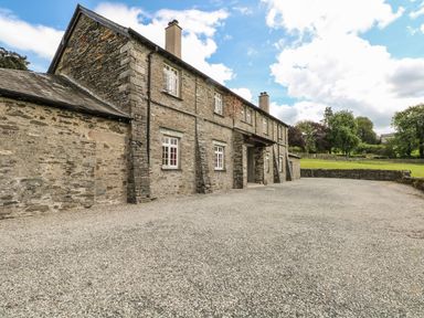 A stone building with multiple windows and chimneys next to a gravel driveway and green lawn at Buttermere in Sawrey near Hawkeshead