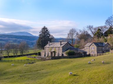 Stone houses surrounded by fenced green fields with grazing sheep and trees in a rural landscape