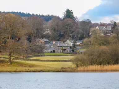 A lake in front of a field with trees and houses in the background at Buttermere Sawrey near Hawkeshead